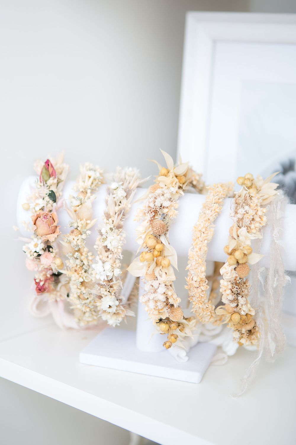 Delicate floral crowns and hair accessories made with dried flowers and pearls displayed on a white shelf.