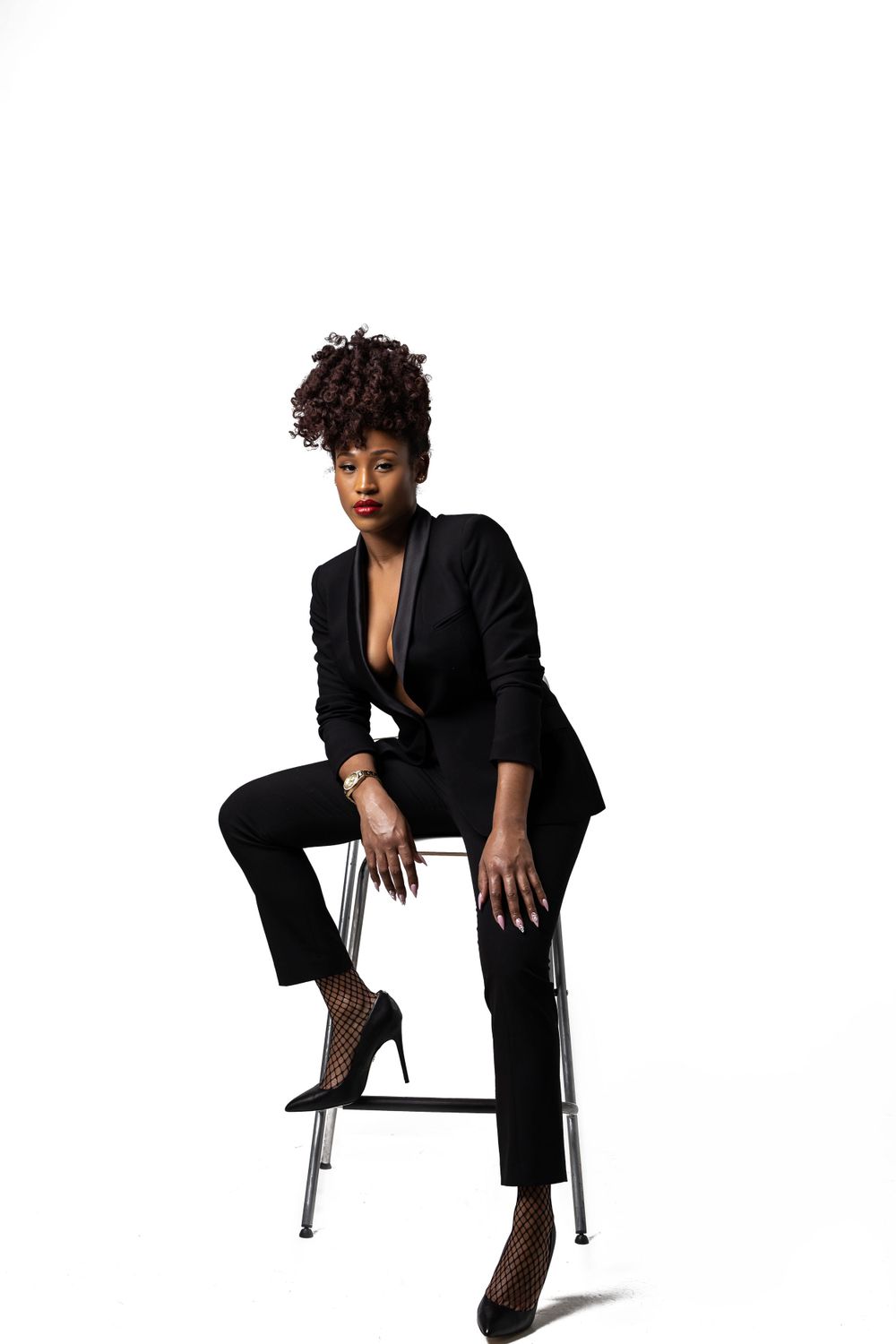 Professional studio portrait featuring a black pantsuit and stiletto heels on a minimalist white background.