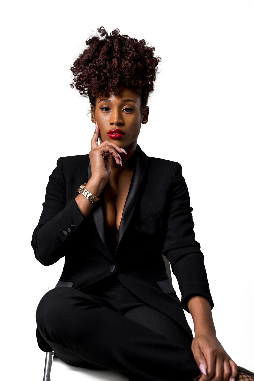 Glamorous studio portrait featuring curly updo, red lips and black blazer on white background.