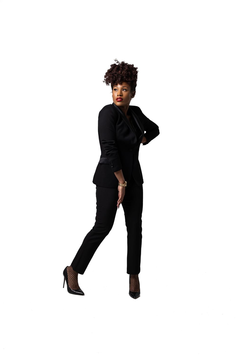 Stylish full-length portrait in black pantsuit with heels against white backdrop.
