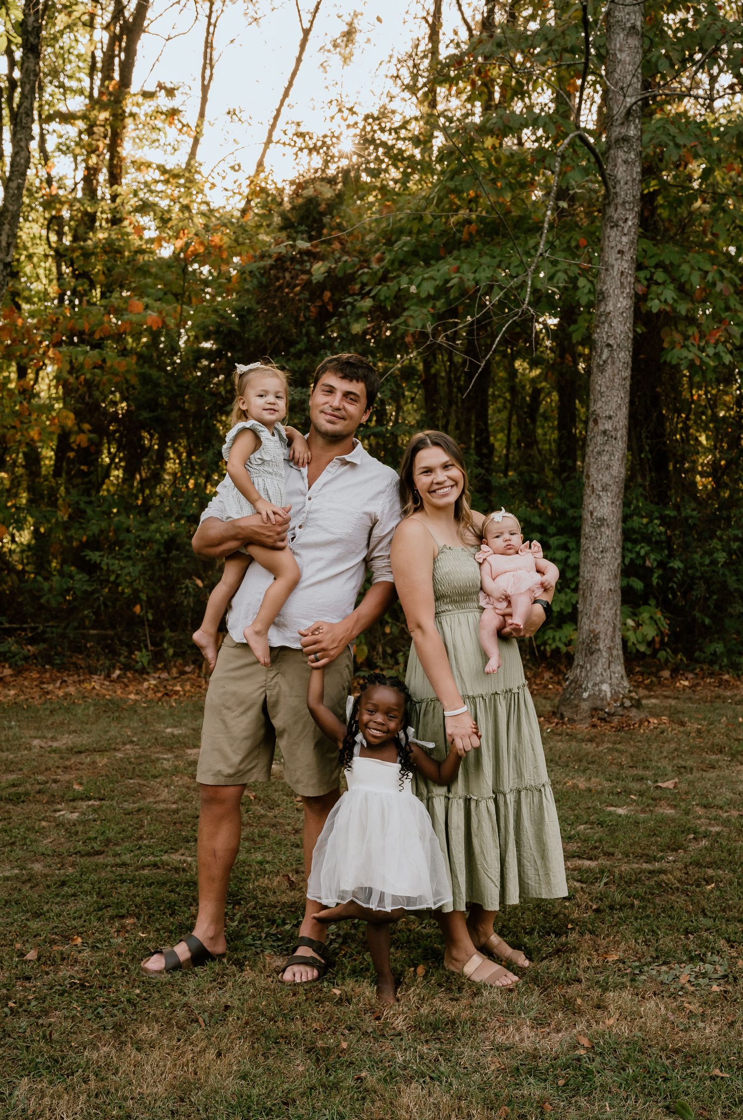 A family of five poses together for a warm sunset portrait in a wooded setting.