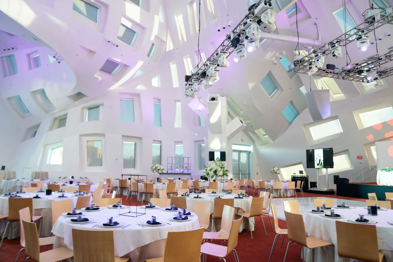 Modern reception venue with geometric skylights creating dramatic lighting effects and round dining tables.