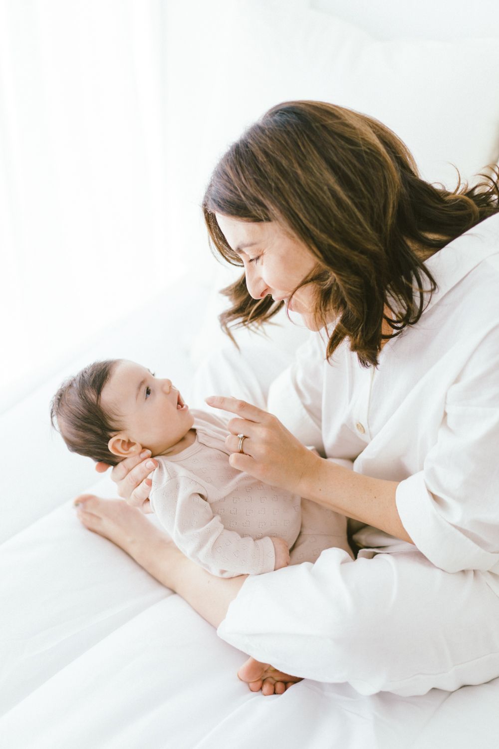 Parent gently touching baby's face during tender moment on white bedding.