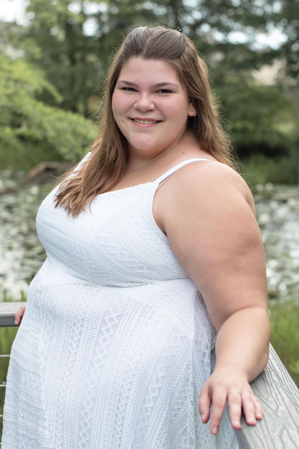Portrait of someone wearing white sleeveless dress against natural outdoor background.