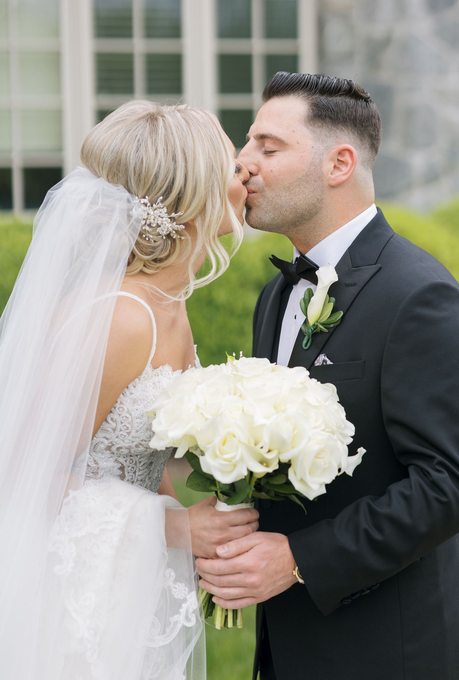 Romantic wedding kiss with bride holding white rose bouquet outdoors.