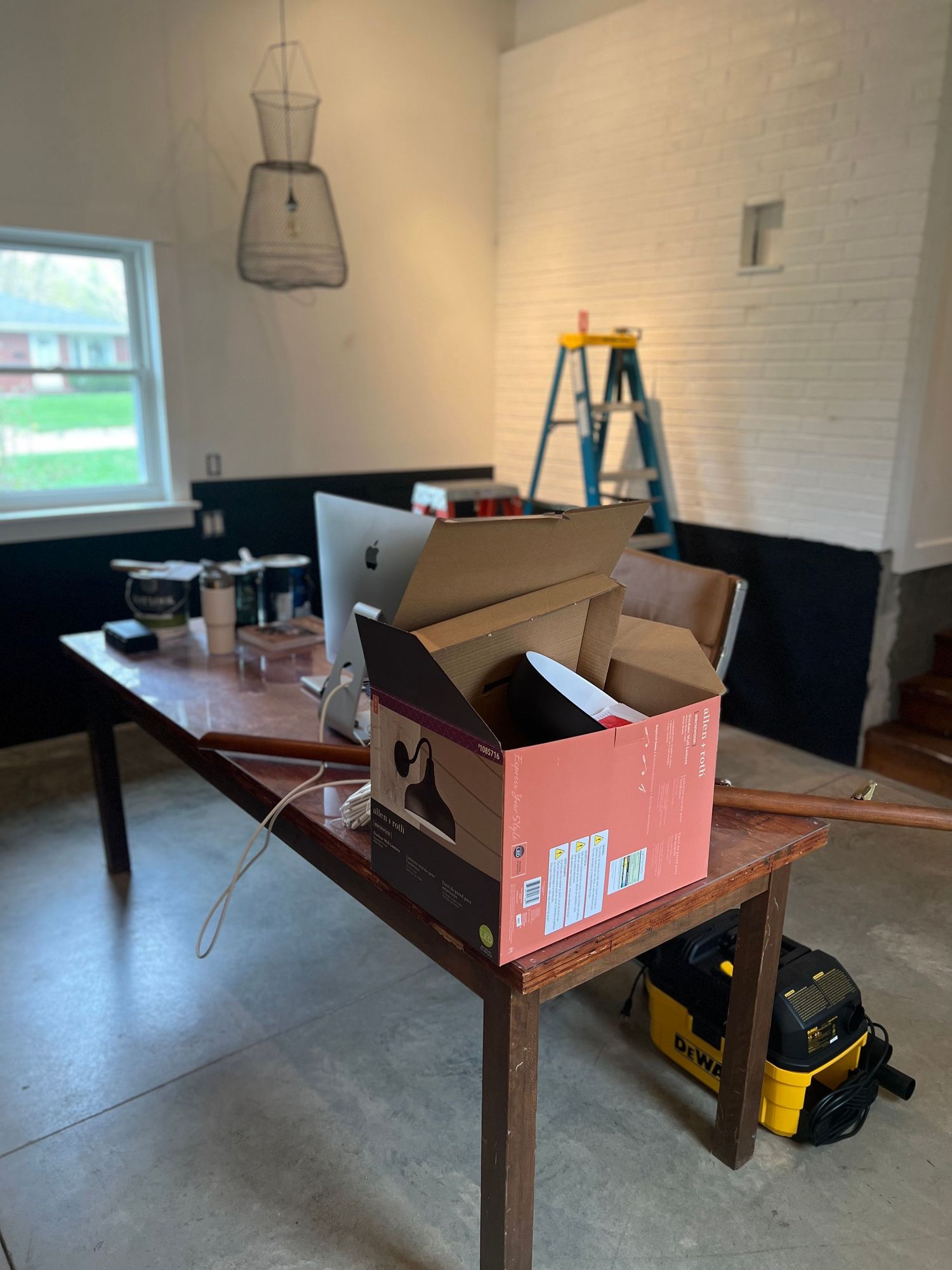 Work desk setup with boxes and computer equipment against white brick wall.