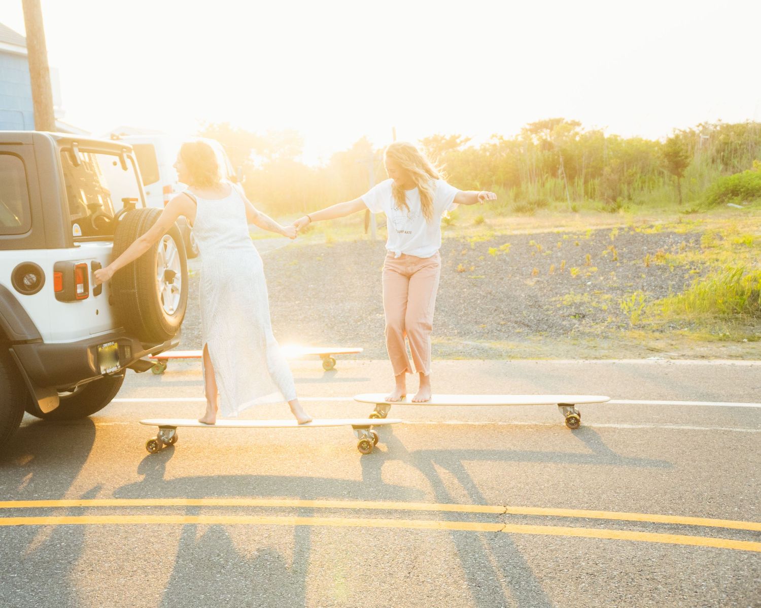 women long boarding behind a jeep at sunset