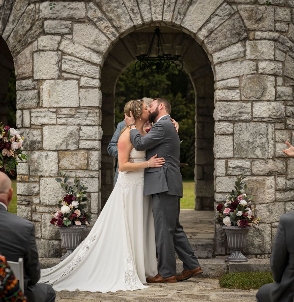 A tender moment shared under a stone archway decorated with pink and white florals.