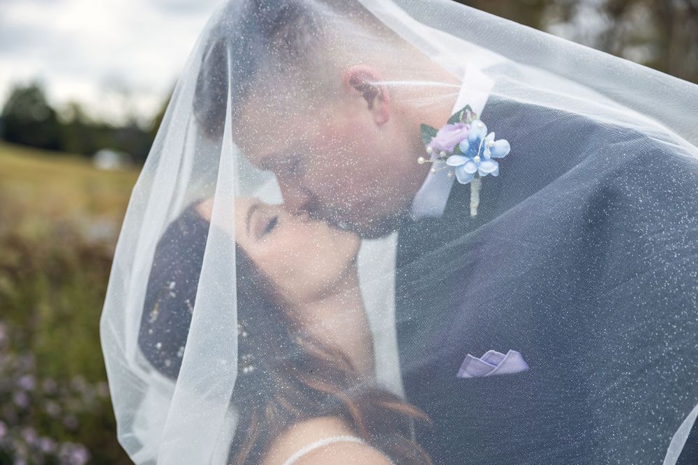 Intimate moment captured under flowing white veil during outdoor wedding ceremony.