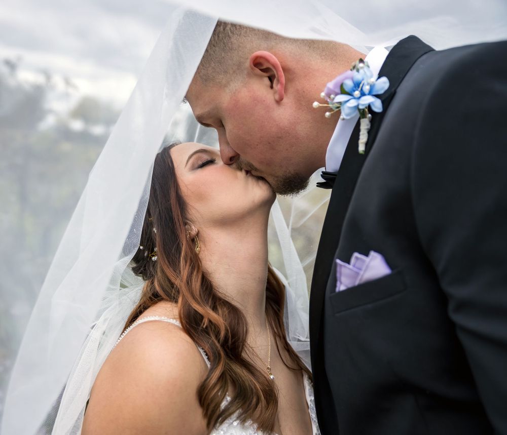 Close-up of wedding couple sharing intimate kiss under white veil.