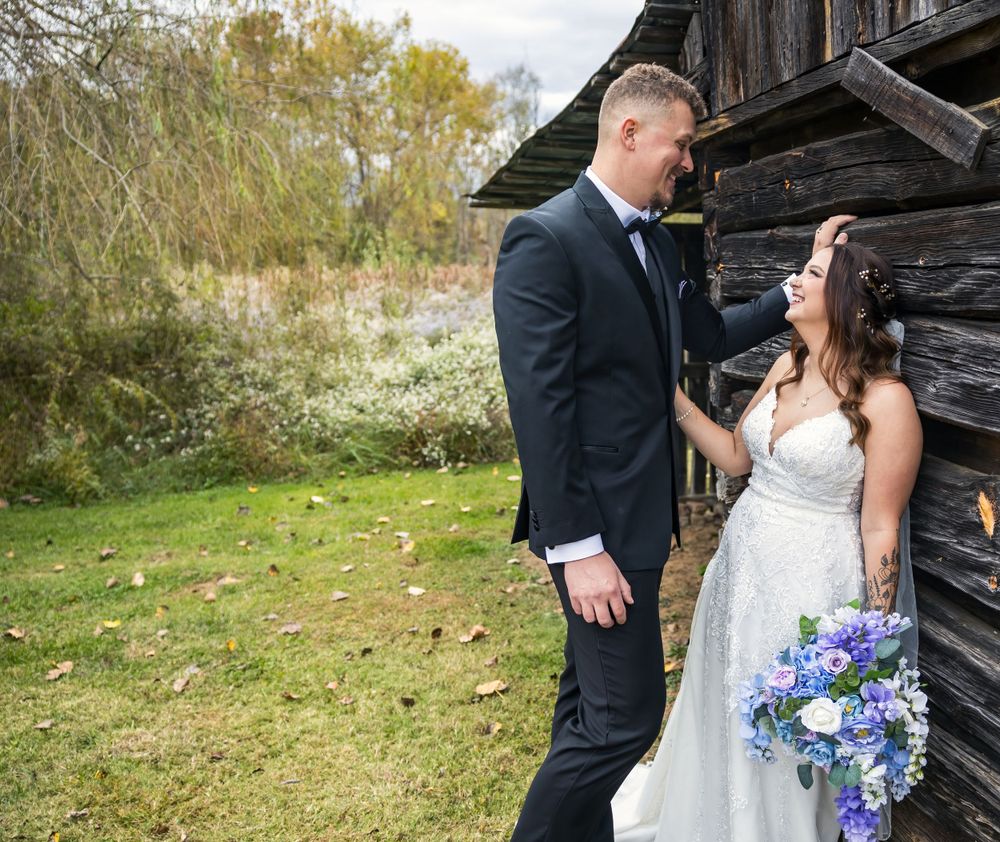 Couple shares tender moment against rustic wooden barn in countryside setting.