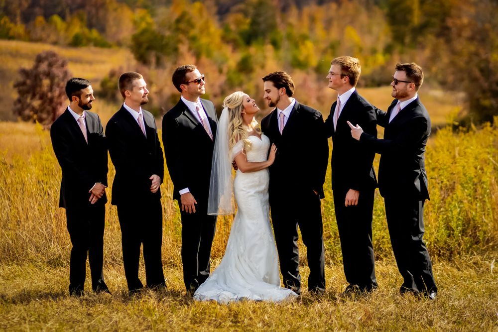 Wedding party poses together in a golden autumn field with mountains in the background.