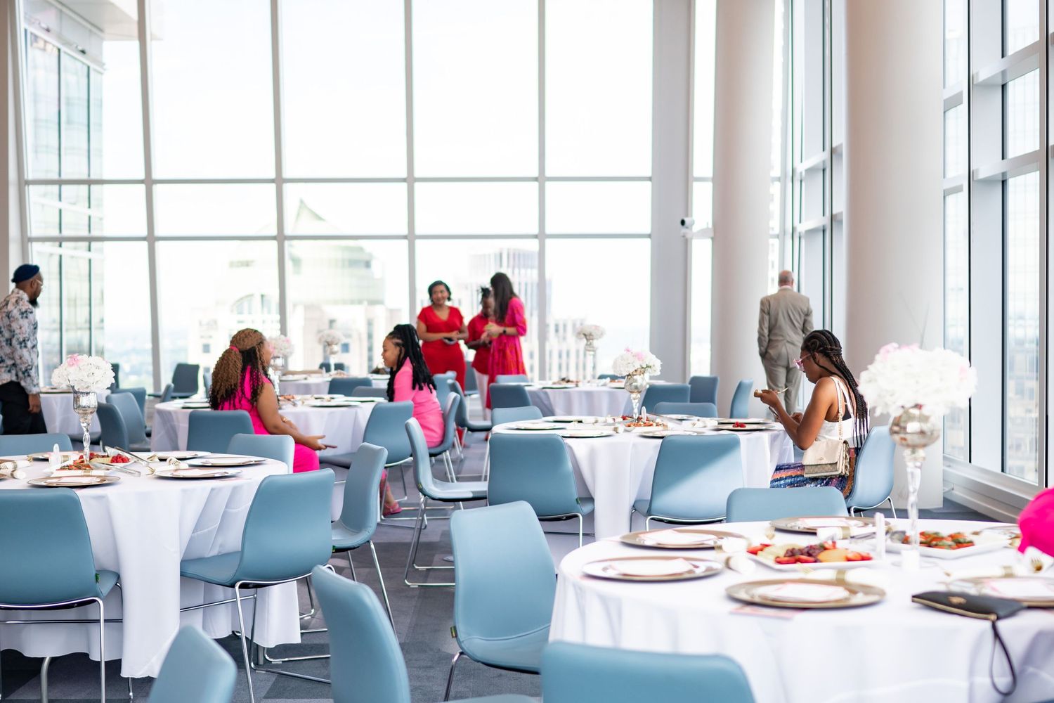 Bright contemporary event space with round tables and blue chairs set for dining.