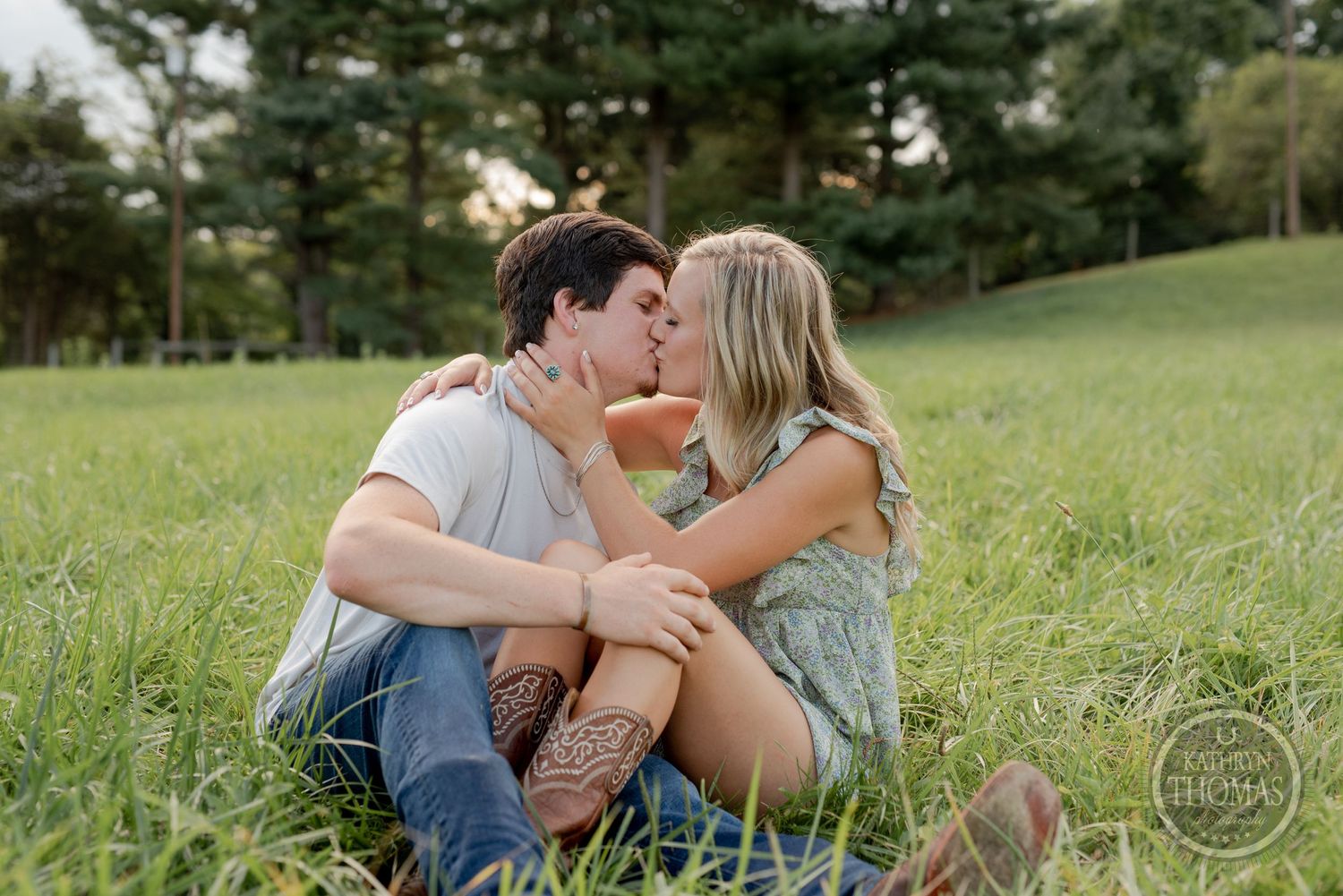 Couple shares intimate moment sitting in sunlit grassy field.