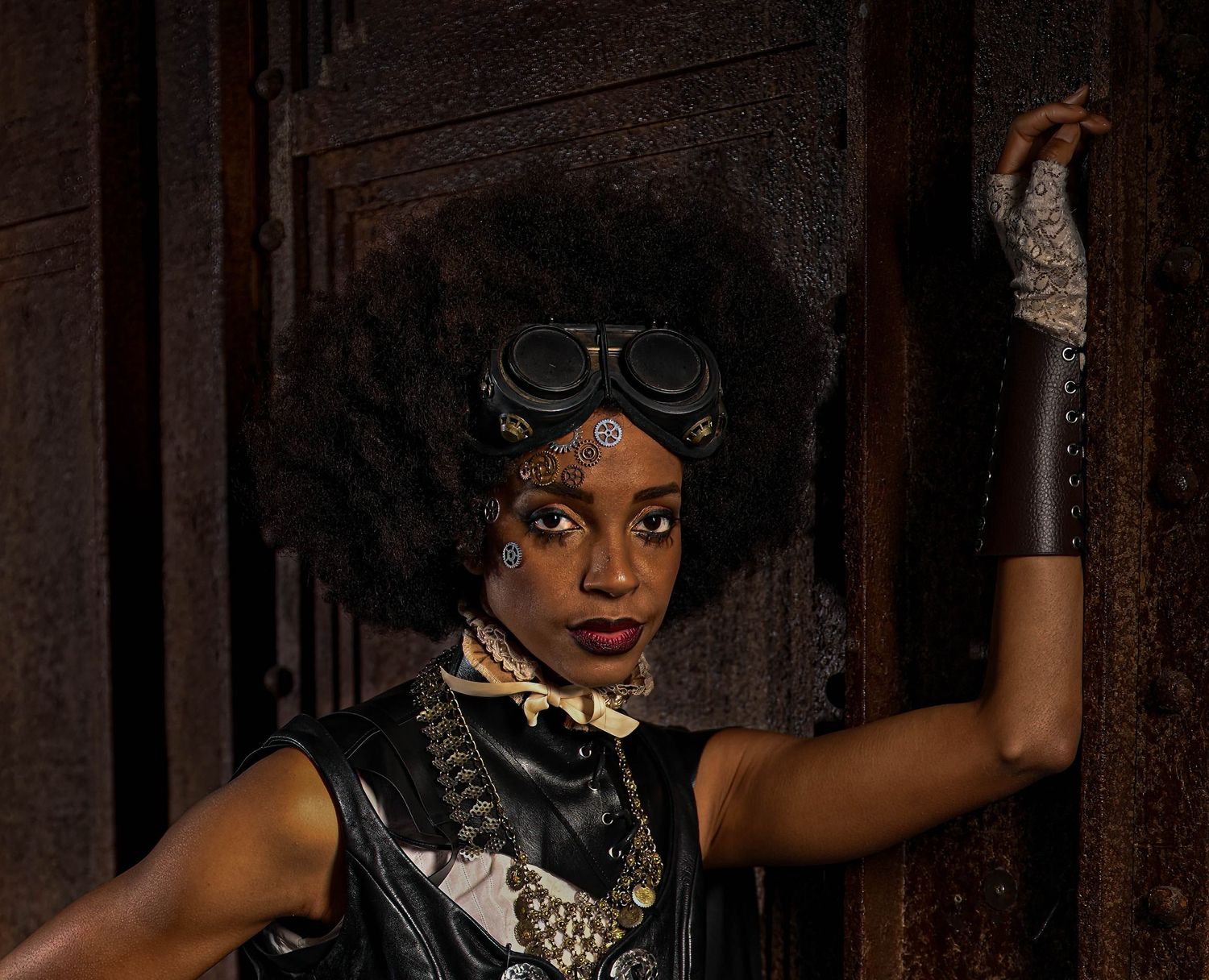 Steampunk-inspired portrait with goggles, afro hairstyle, and industrial accessories.