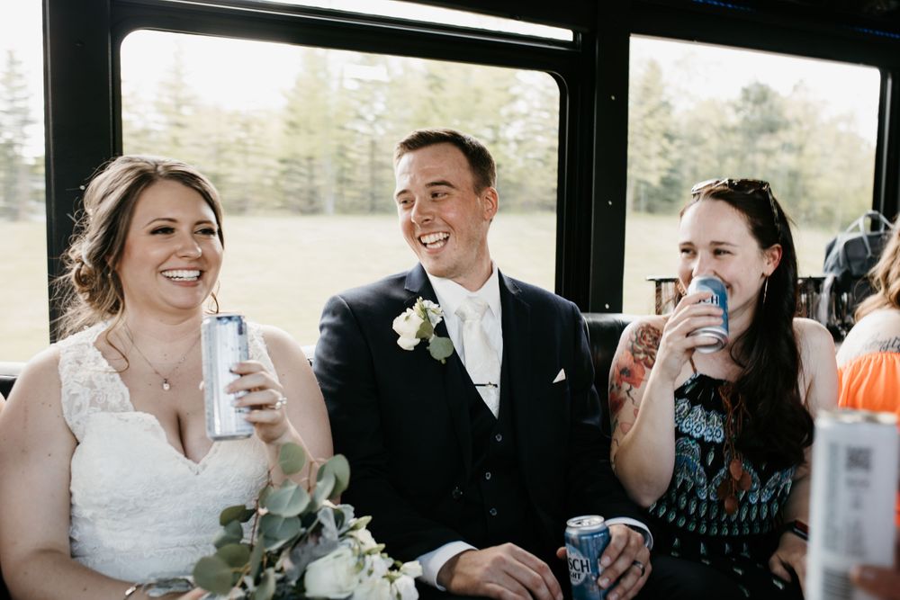 Bride, groom, and guest laughing together on wedding party bus.