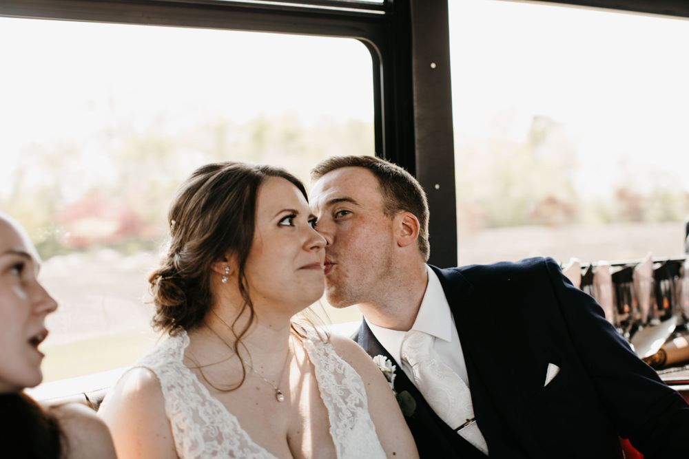 Groom kissing bride on cheek during party bus wedding celebration.