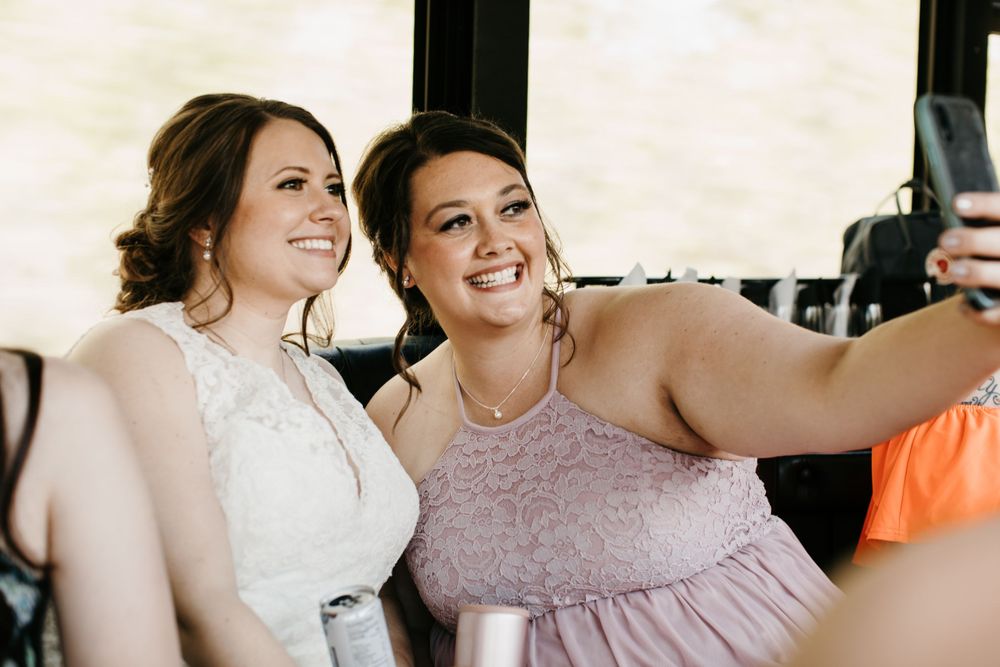 Bride and bridesmaid taking selfie together on wedding party bus.