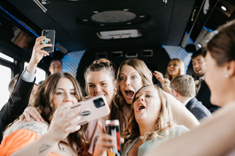 Excited wedding guests taking group selfie on party bus.