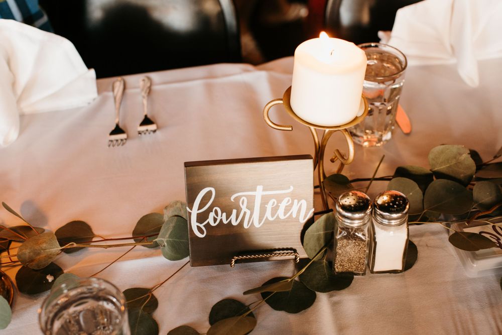 Wedding table number fourteen sign with candle, eucalyptus greenery, and salt and pepper shakers.