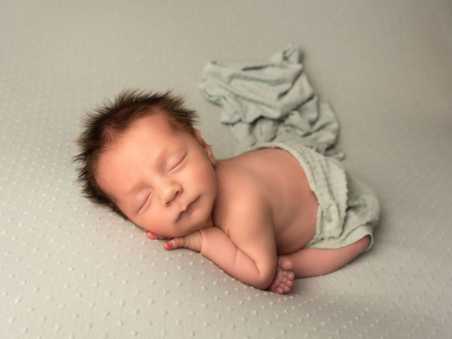 baby boy with fluffy hair sleeping on textured sage blanket by professional newborn photographer in Doncaster.
