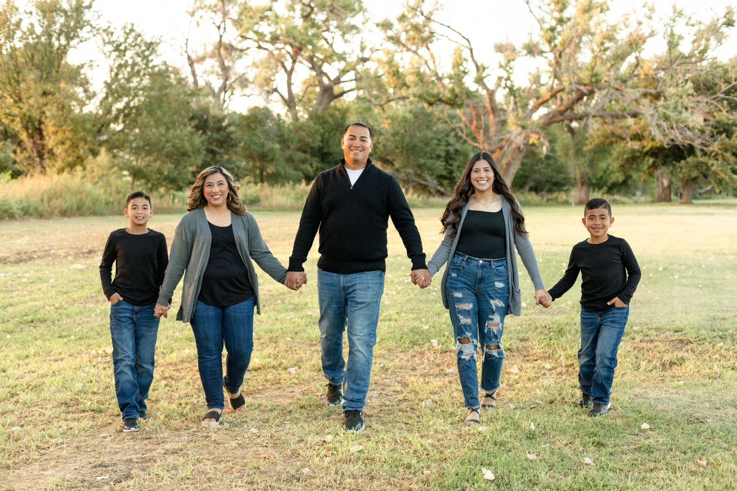 Family of five walking together holding hands in an outdoor field during golden hour.