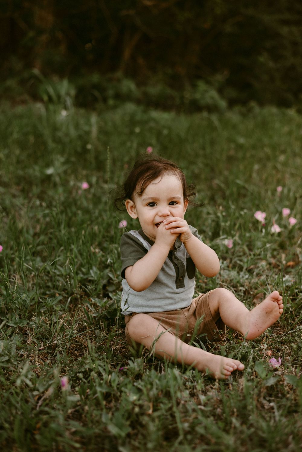 Sweet candid moment of toddler sitting in grass among blooming wildflowers.