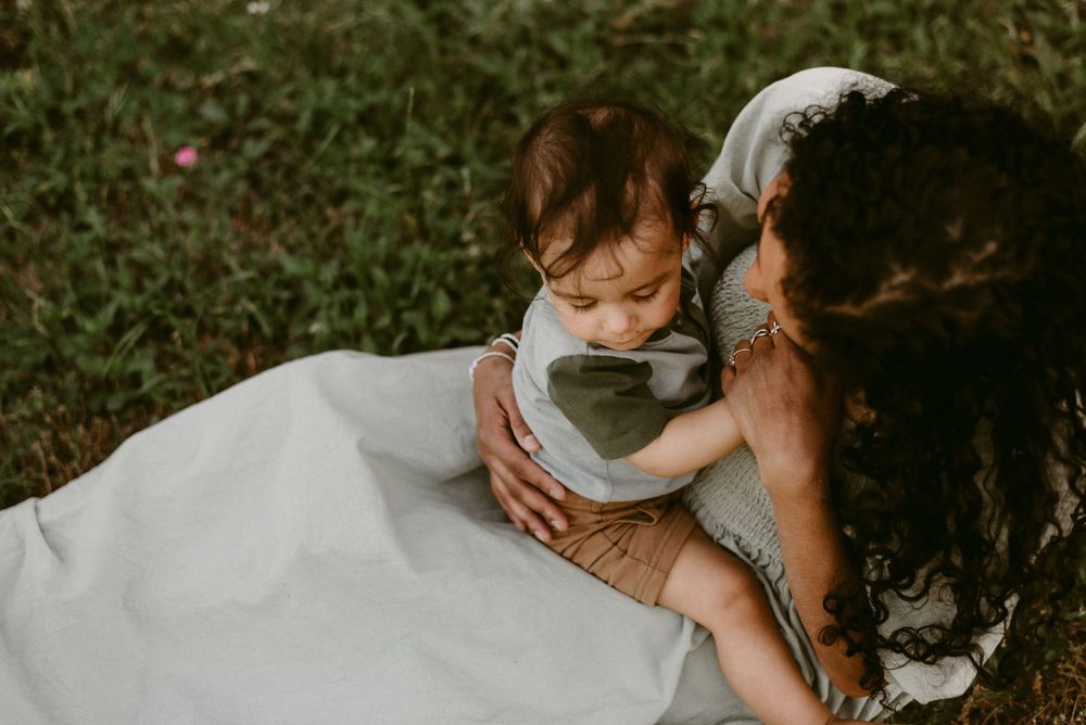 Parent in light dress shares intimate moment with toddler on grassy ground.