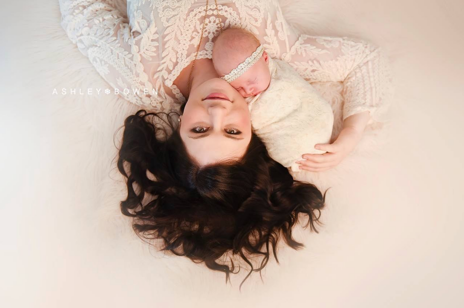 Overhead view of mother lying down with newborn baby on white background.