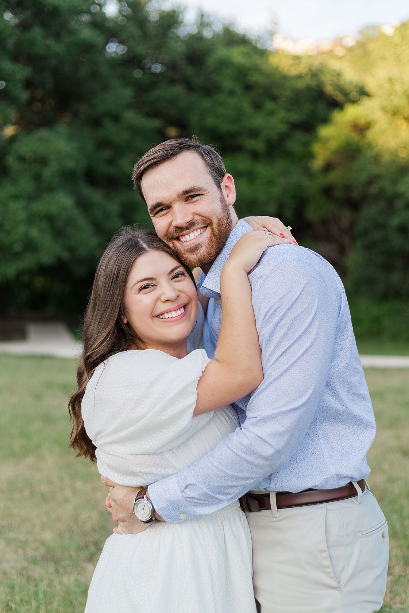 Couple sharing warm embrace and genuine smiles in casual outdoor portrait.