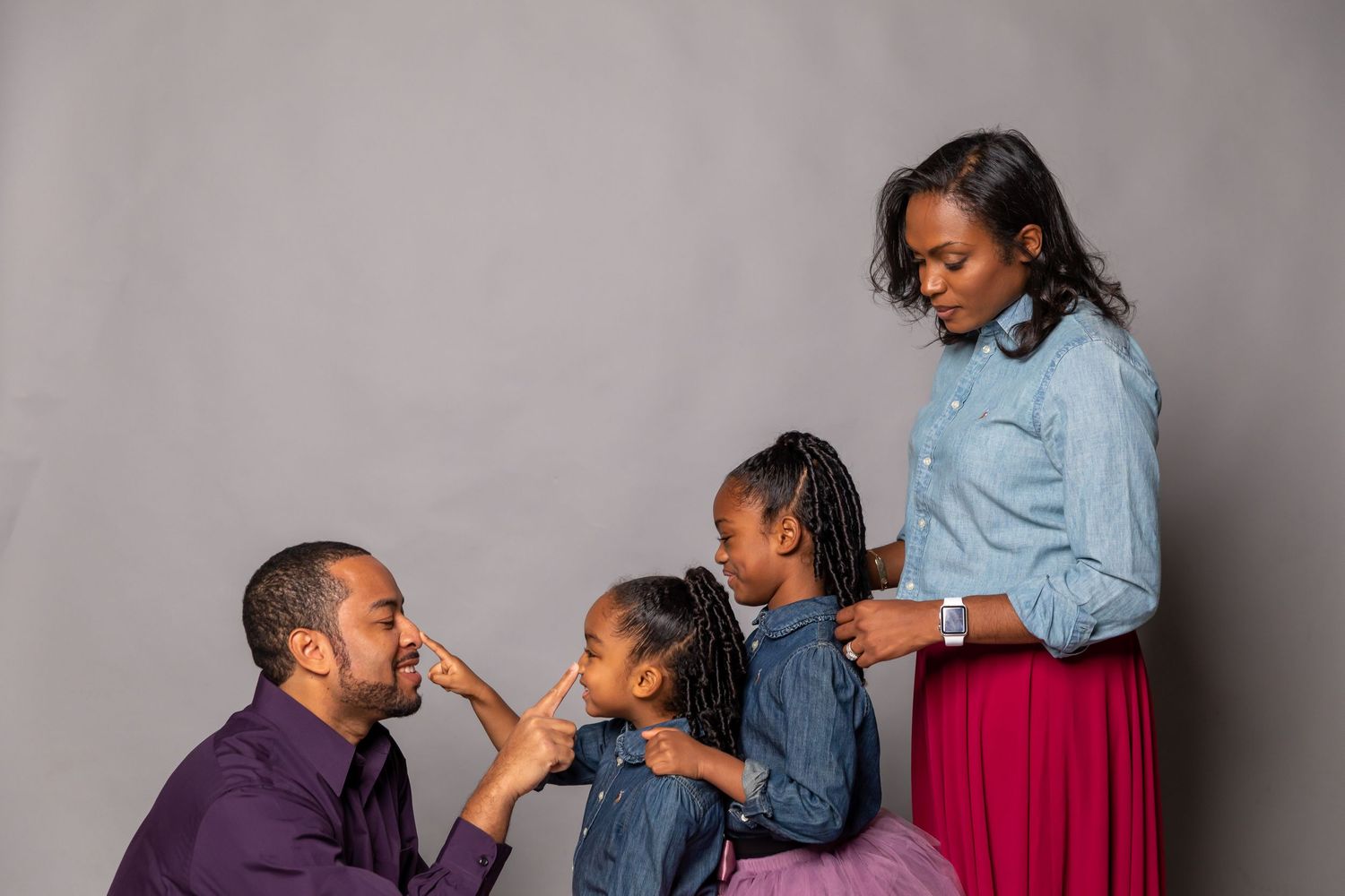 Black family of four interacting playfully during professional studio portrait session with gray background.