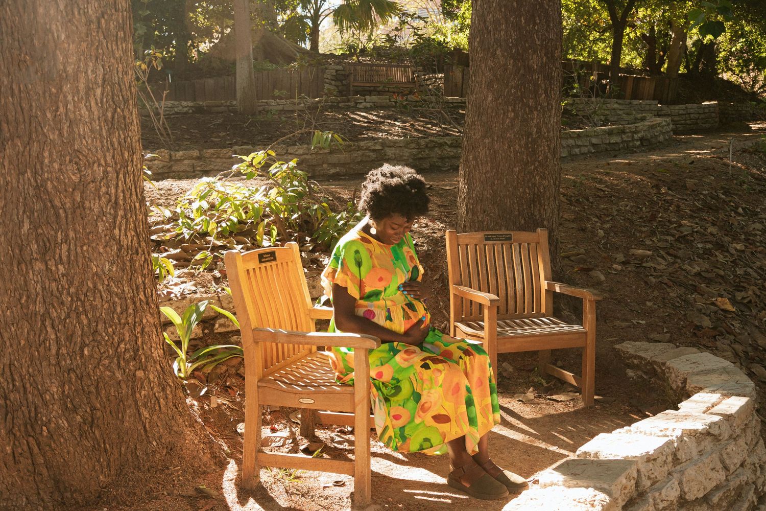 Person in floral dress seated on wooden chairs in dappled sunlight garden setting.