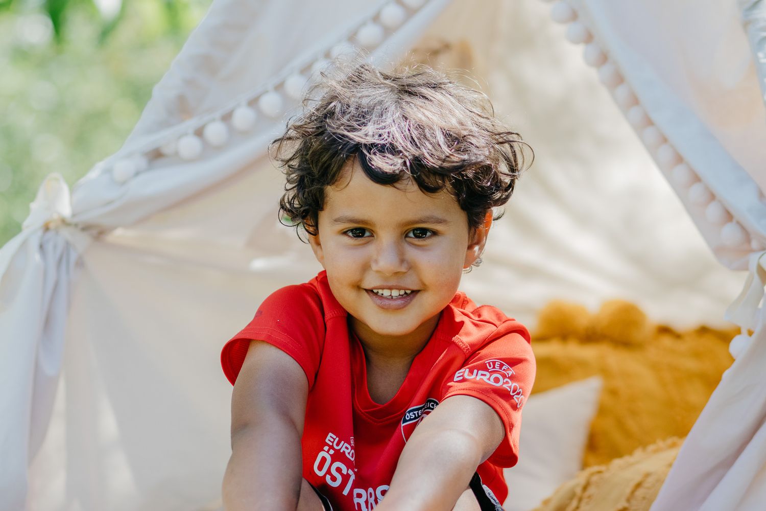 Children playing in a white teepee tent with yellow cushions outdoors.