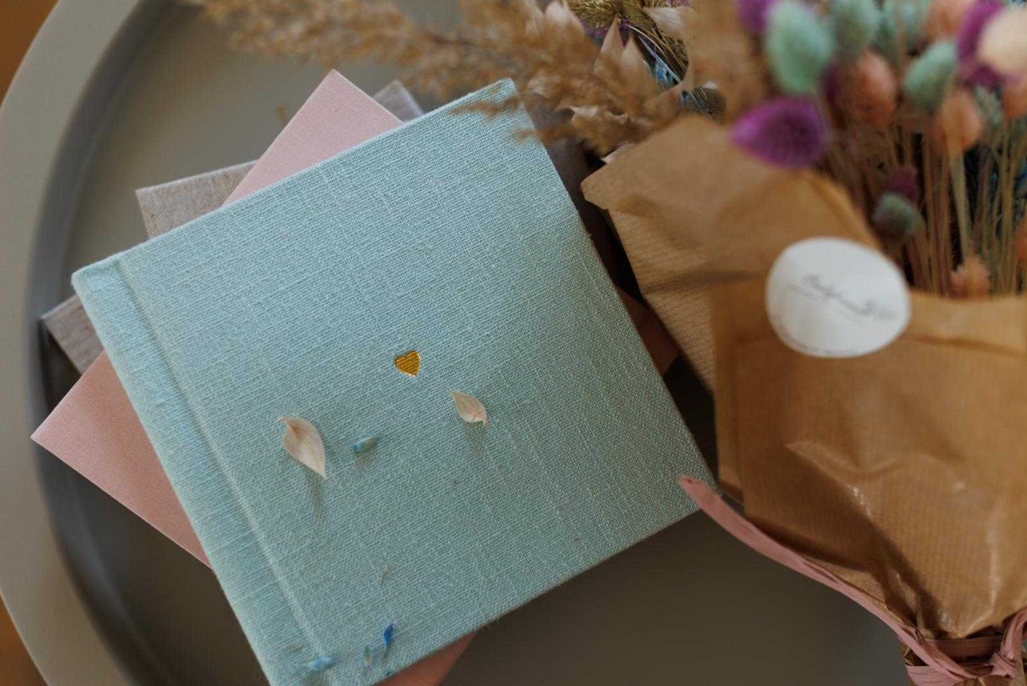 Mint green and pink photo albums with dried flowers on a gray surface.