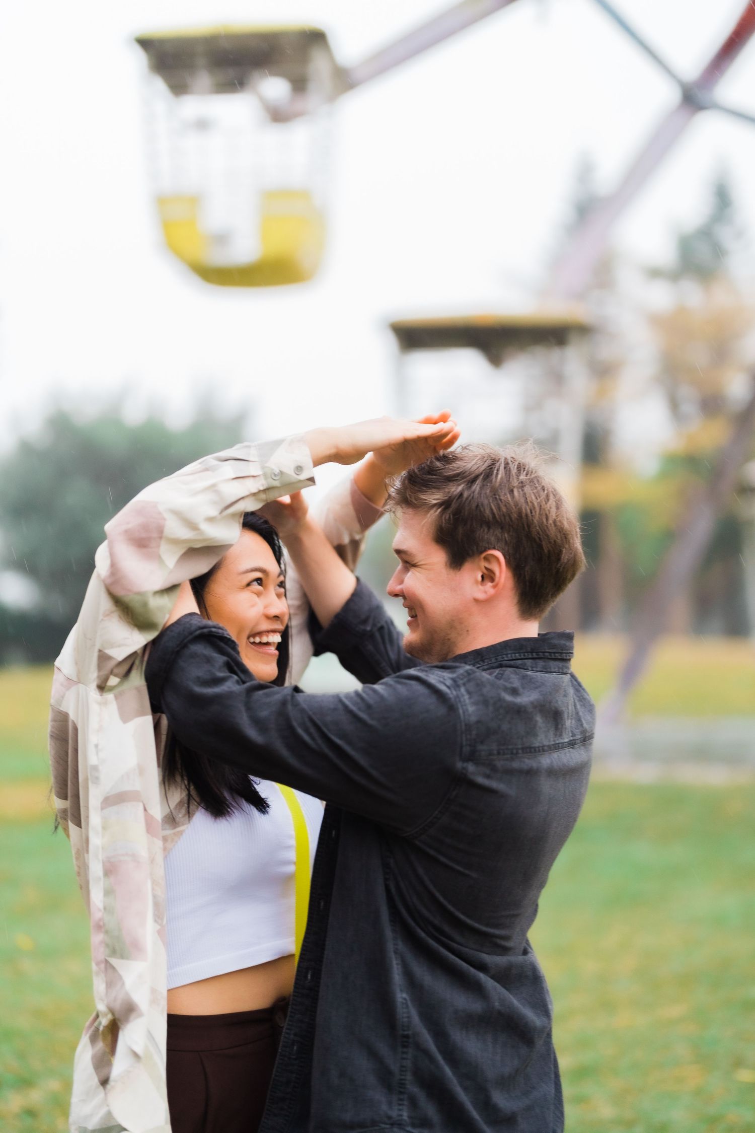 Playful couple sharing lighthearted moment at amusement park with rides in background.