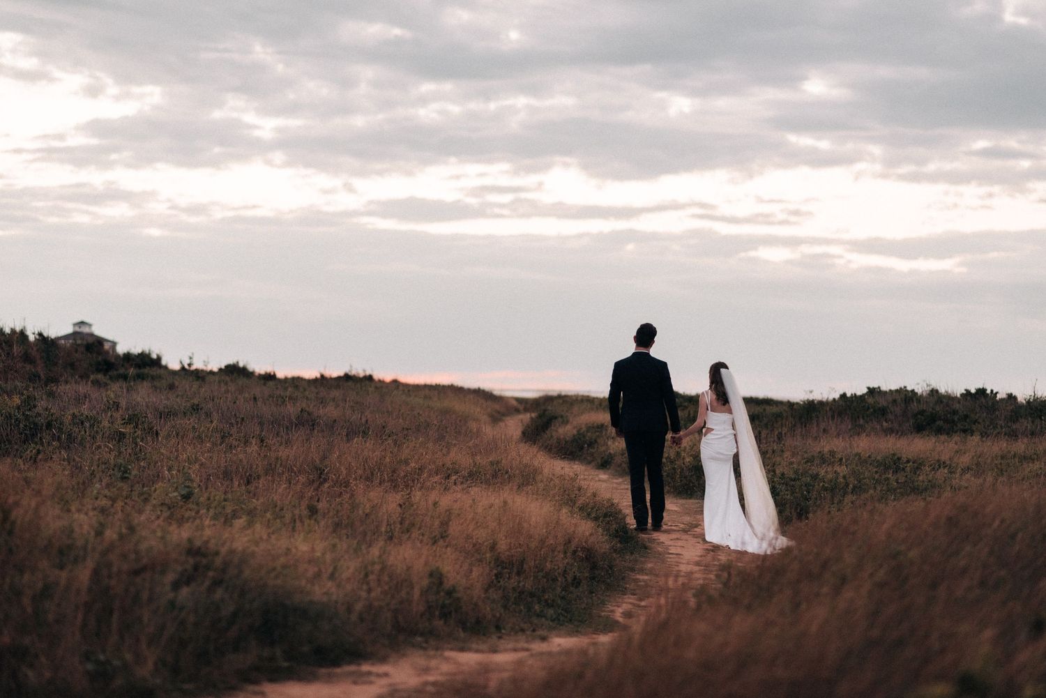 Silhouetted couple walking along hilltop path during sunset.