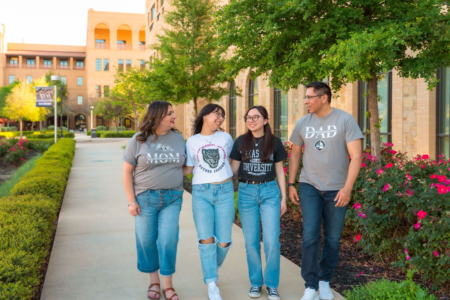 Albertvphotos, family of 4 hold hands walking along sidewalk of Texas A&m