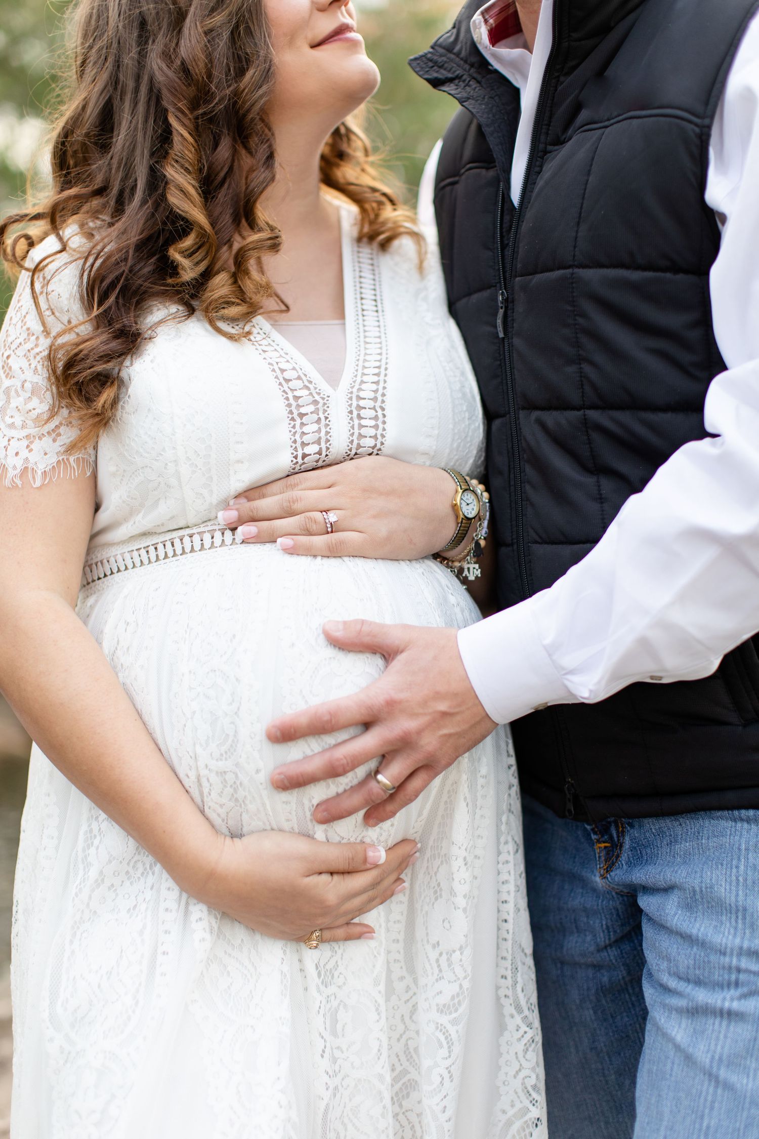 Close-up of hands cradling pregnant belly in white lace dress.