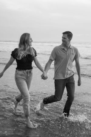 Playful couple splashing in ocean waves at the beach in black and white.