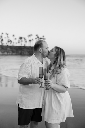 Couple sharing champagne and kiss on beach at sunset.