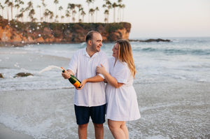 Couple walking along tropical beach with palm trees at sunset.