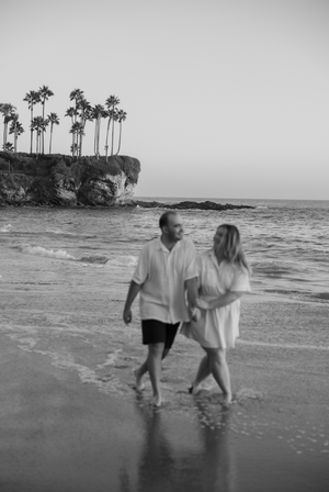 Black and white photo of couple walking along tropical beach with palm trees.