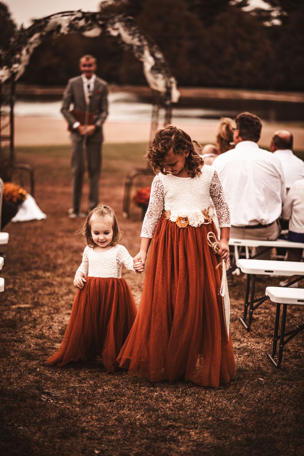 Two attendees in matching burgundy dresses stand at outdoor wedding ceremony.