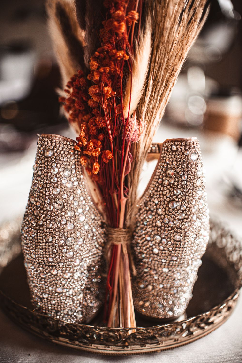 Sparkly bridal shoes displayed with dried floral bouquet on decorative plate.