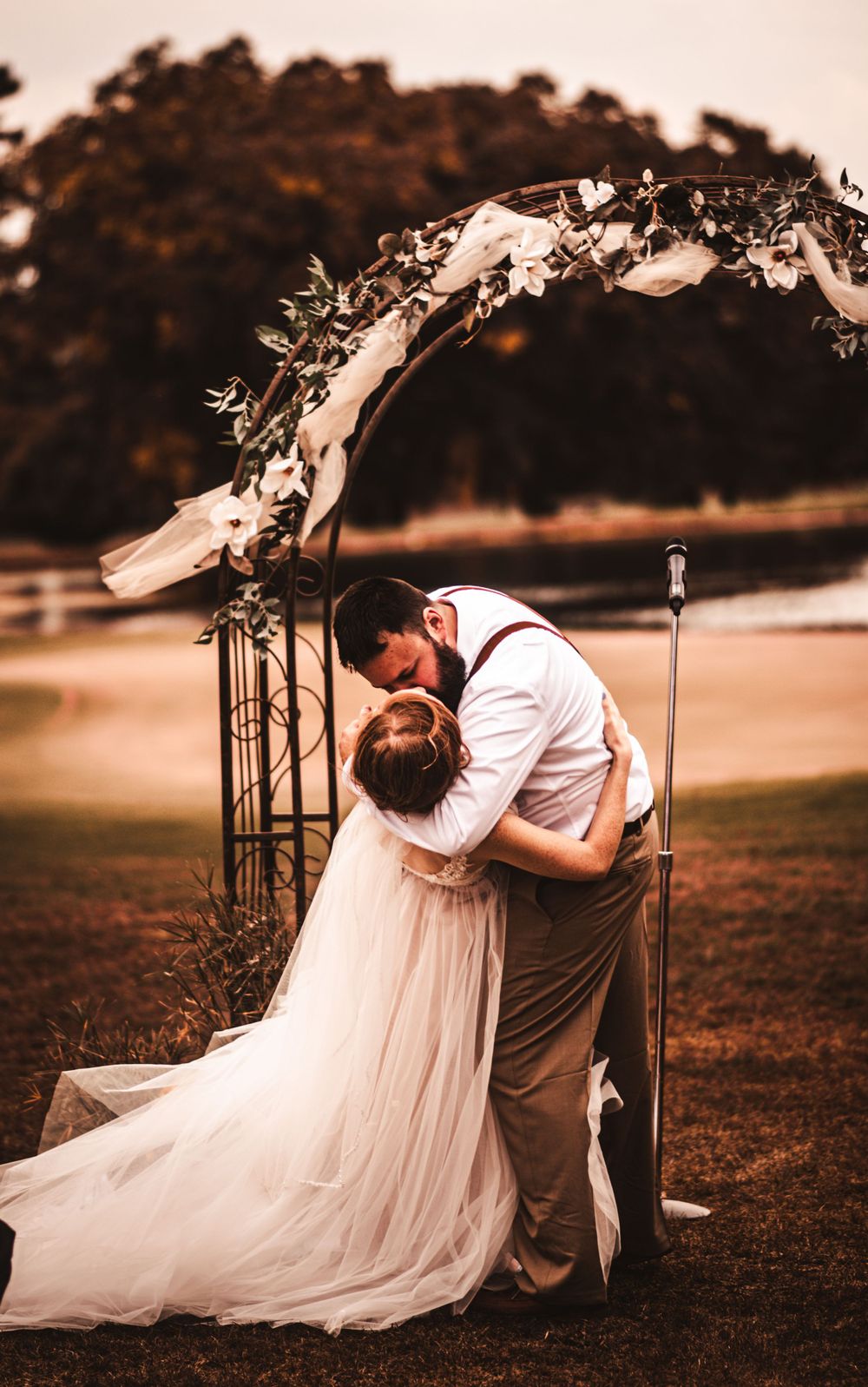Romantic moment captured under a floral arch with flowing white wedding dress at sunset.