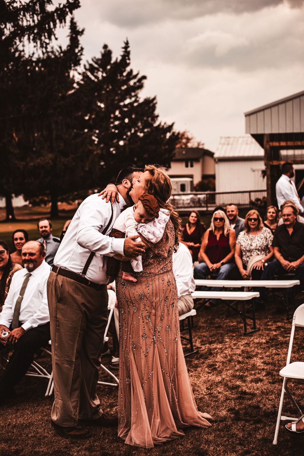 Sweet moment during outdoor wedding reception with white chairs and guests in background.