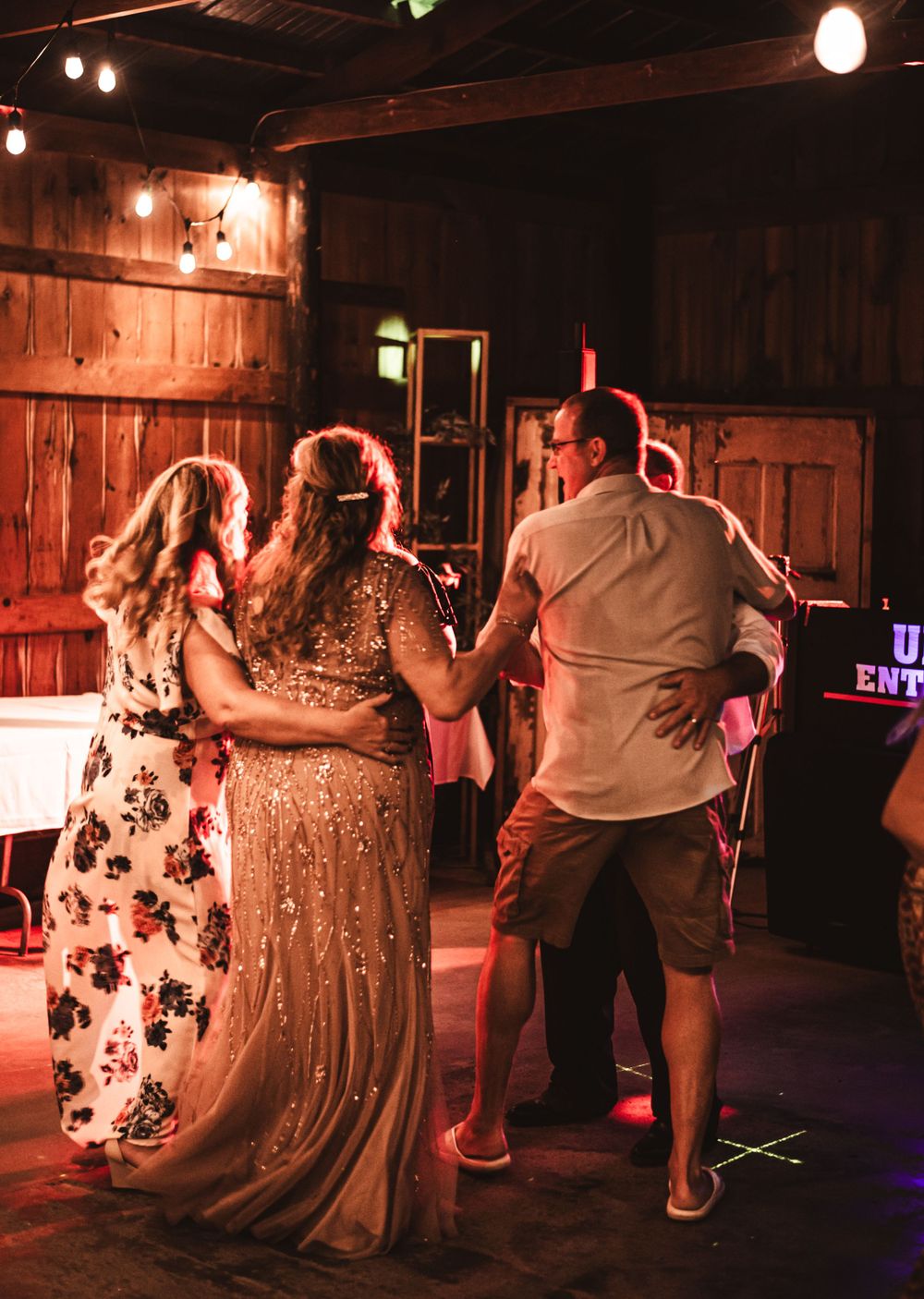 Wedding guests dancing at rustic barn reception with warm lighting.