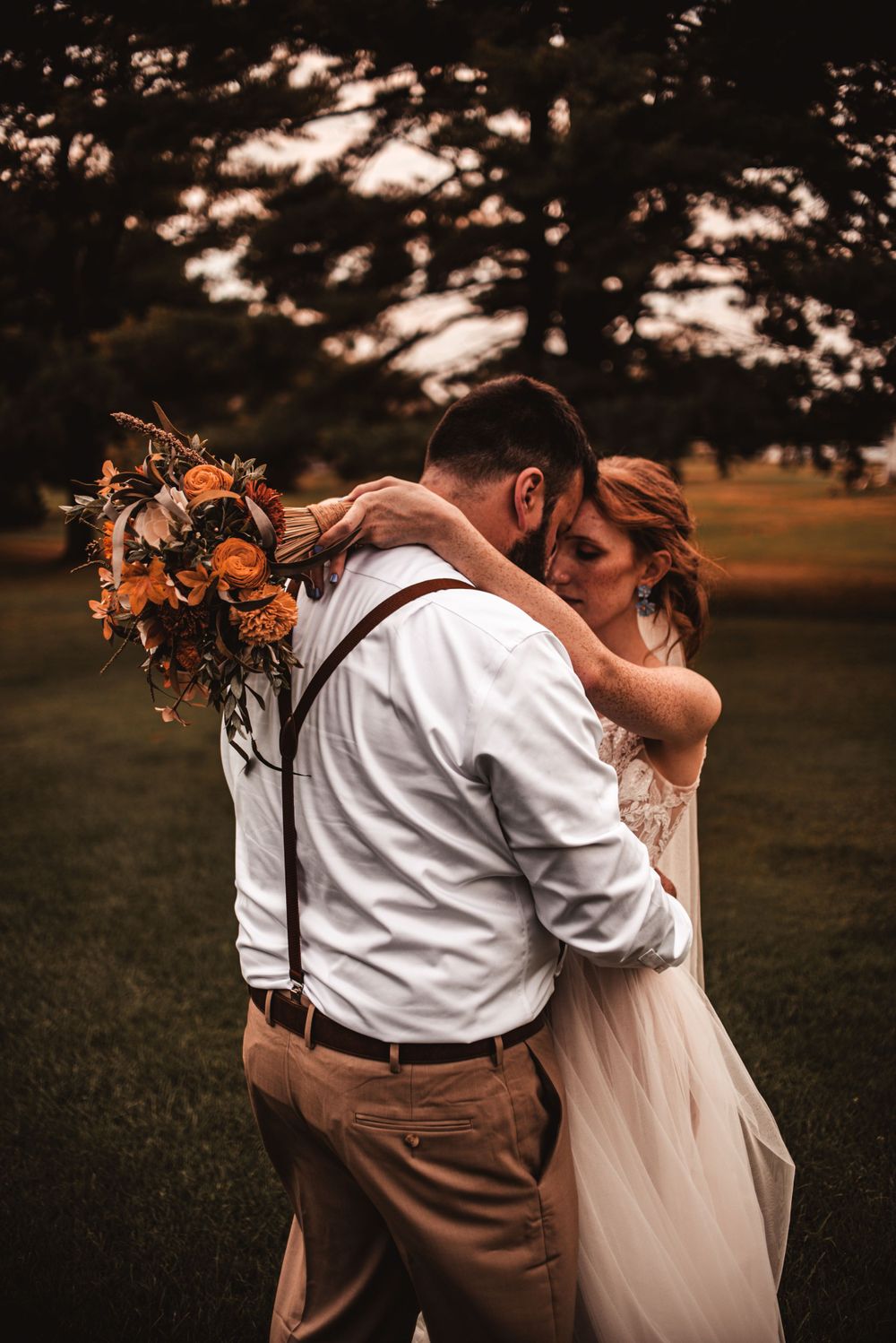 An intimate moment between newlyweds with autumn-colored florals against a shadowy forest backdrop.