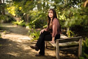 Person sitting on wooden bench in park with autumn foliage background.