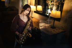 Musician playing saxophone in moody room with warm lamp lighting.